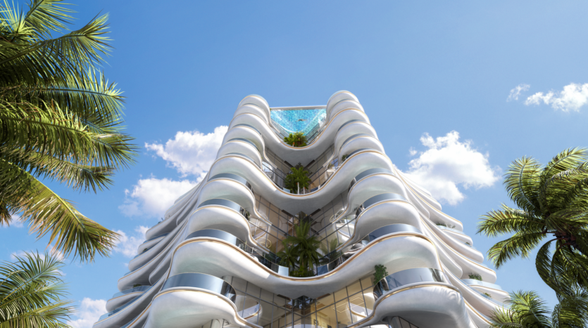 Le Beach Walk Grand est un bâtiment moderne au design ondulé avec des balcons en verre et une végétation luxuriante à chaque étage. Une piscine sur le toit orne le sommet, tandis qu'un ciel clair avec quelques nuages et des palmiers encadrent magnifiquement cette merveille architecturale.