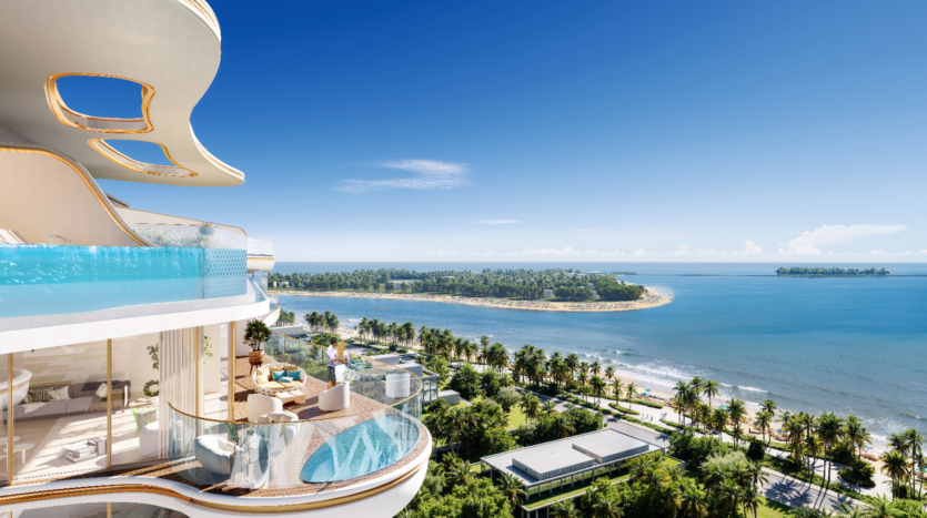 Le Beach Walk Grand est un luxueux complexe balnéaire doté d'un élégant bâtiment blanc avec une piscine sur le balcon donnant sur l'océan bleu. Des palmiers parsèment le paysage sous un ciel clair, avec une péninsule de sable visible au loin.