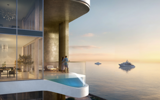 Un couple se tient sur un balcon moderne avec une balustrade en verre au LIV Maritime, surplombant une mer sereine au coucher du soleil. Trois yachts glissent au loin. À travers les grandes fenêtres de l'appartement de luxe, vous pouvez voir une décoration élégante qui complète parfaitement le décor maritime tranquille.