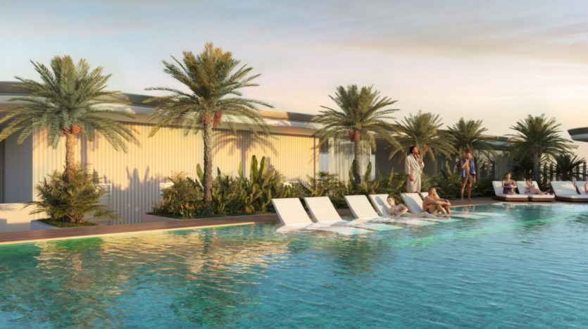 Un groupe de personnes se détend au bord d'une piscine extérieure moderne, nichée dans une crique sereine entourée de palmiers. Des chaises longues bordent le bord de la piscine tandis que le ciel du coucher de soleil projette une lueur chaleureuse sur ce paradis Edition 3.