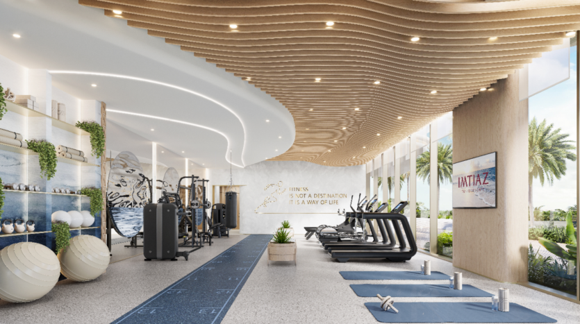 Une salle de sport moderne à Sunset Bay dispose de panneaux de plafond en bois ondulés, de grandes fenêtres et de palmiers à l'extérieur. La salle comprend des tapis de course, des appareils de fitness, des tapis de yoga et des ballons d'exercice. Une citation de motivation orne le mur, tandis qu'un écran de télévision affiche « INTATAX ».