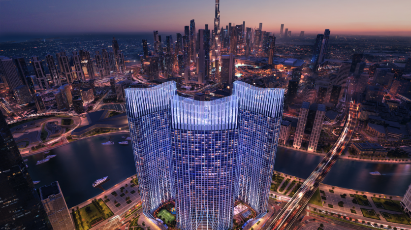 Vue aérienne d'un paysage urbain au crépuscule, avec un gratte-ciel moderne à l'architecture incurvée illuminée de lumières bleues. Les bâtiments et les voies navigables environnantes reflètent les lumières de la ville, avec un horizon urbain dense en arrière-plan.