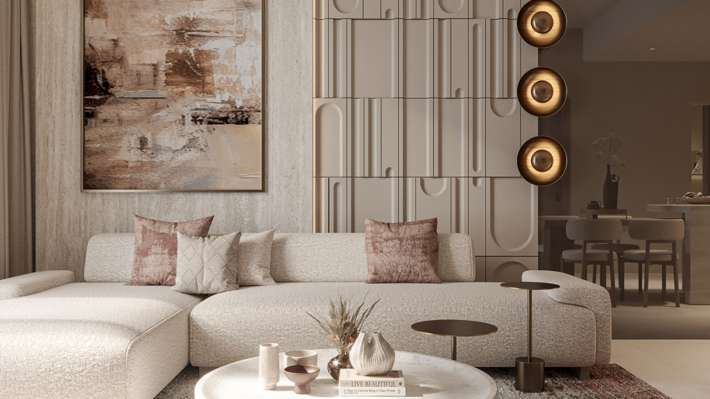 A modern living room features a large beige corner sofa with patterned cushions, a round coffee table with decorative objects and abstract artwork on the wall. Circular wall sconces provide warm lighting, and a kitchenette is visible in the background.