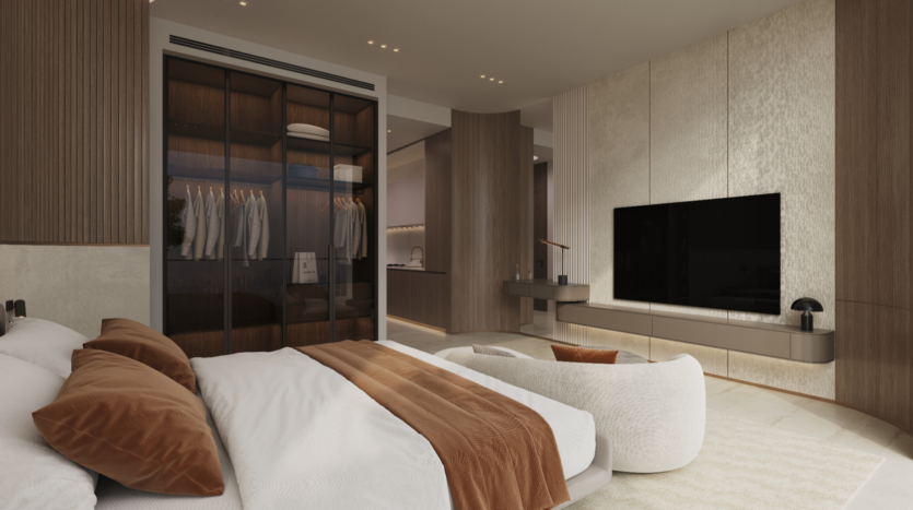 Une chambre moderne inspirée du style Binghatti Elite avec une palette neutre comprend un grand lit habillé de draps blancs et d'oreillers couleur rouille. Une télévision murale et une chaise confortable se trouvent en face. Le placard à portes vitrées, éclairé par un éclairage chaleureux, ajoute une touche élégante au décor.