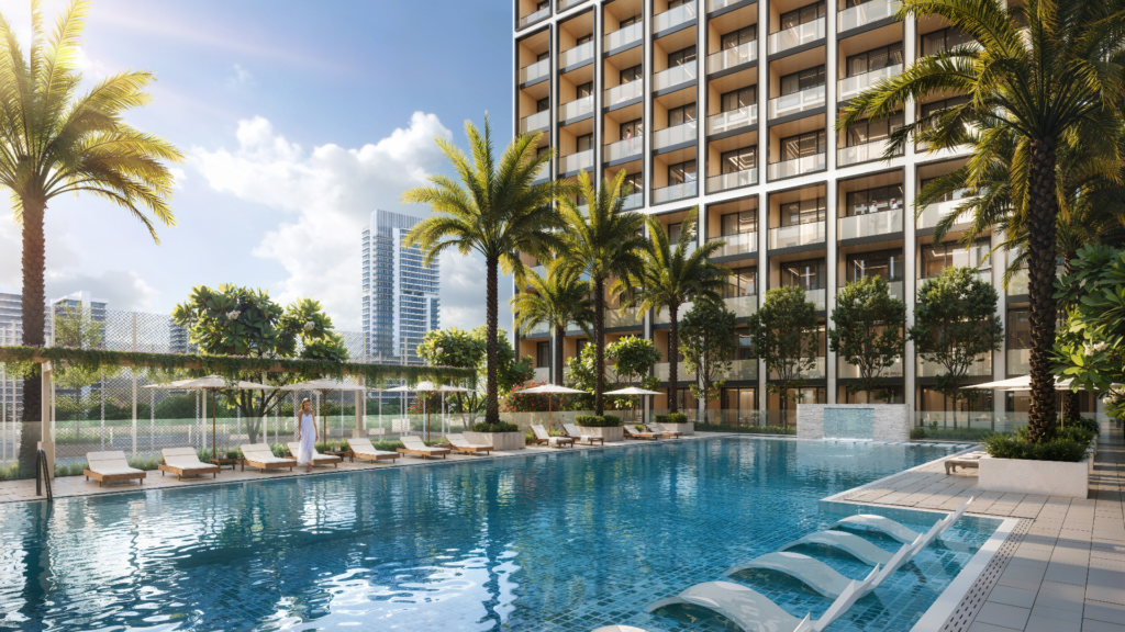 Une grande piscine extérieure, dégageant une ambiance d'élite, est entourée de palmiers et de chaises longues devant un grand immeuble d'appartements Binghatti. Le ciel est clair et ensoleillé, avec un horizon urbain moderne en arrière-plan. Une personne se tient debout au bord de la piscine.