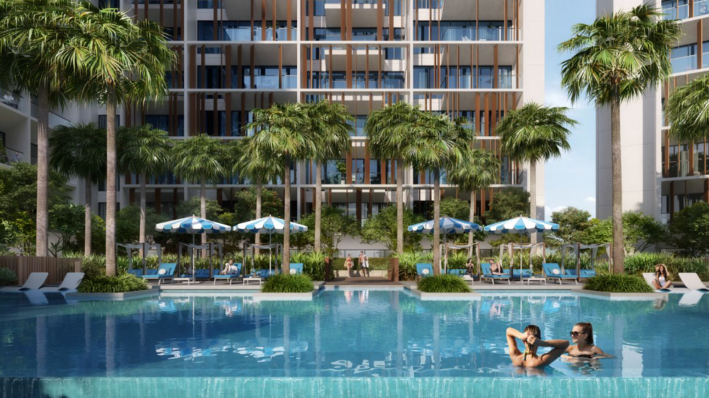 Le Parkfive, un complexe d'appartements moderne avec palmiers et chaises longues, entoure une grande piscine. Deux personnes peuvent se détendre dans l'eau tandis que des parasols bleus et blancs offrent de l'ombre à ceux qui sont assis au bord de la piscine.