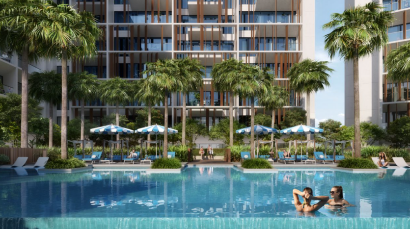 Le Parkfive, un complexe d'appartements moderne avec palmiers et chaises longues, entoure une grande piscine. Deux personnes peuvent se détendre dans l'eau tandis que des parasols bleus et blancs offrent de l'ombre à ceux qui sont assis au bord de la piscine.