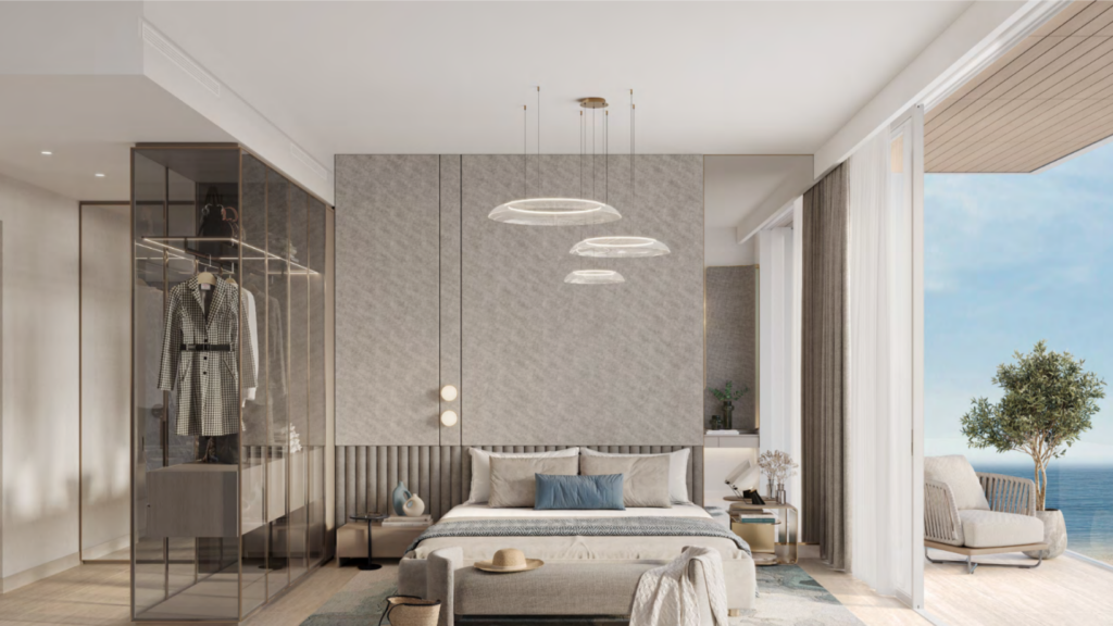 Chambre moderne avec un grand lit, une armoire en verre et un coin salon. Des suspensions sont suspendues au plafond. Une porte coulissante s'ouvre sur un balcon avec vue sur l'océan d'Ellington Cove. Les tons terreux et la décoration minimaliste créent une atmosphère sereine.