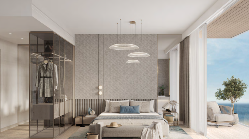 Chambre moderne avec un grand lit, une armoire en verre et un coin salon. Des suspensions sont suspendues au plafond. Une porte coulissante s'ouvre sur un balcon avec vue sur l'océan d'Ellington Cove. Les tons terreux et la décoration minimaliste créent une atmosphère sereine.