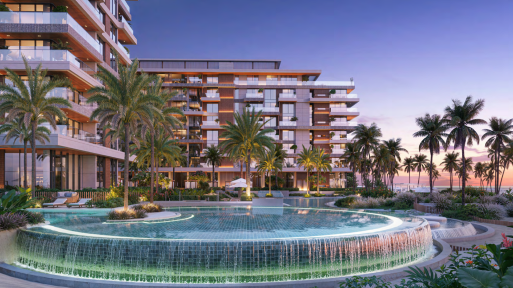 À Ellington Cove, un complexe hôtelier luxueux dévoile au coucher du soleil un bâtiment moderne avec des balcons entourés de grands palmiers. Au premier plan, une grande piscine à débordement circulaire et illuminée avec de l'eau en cascade complète le décor vibrant d'un ciel coloré.