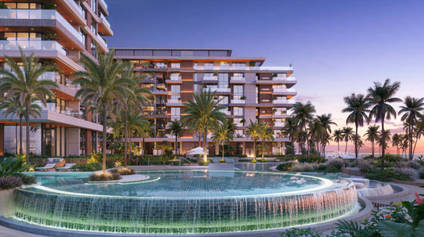 À Ellington Cove, un complexe hôtelier luxueux dévoile au coucher du soleil un bâtiment moderne avec des balcons entourés de grands palmiers. Au premier plan, une grande piscine à débordement circulaire et illuminée avec de l'eau en cascade complète le décor vibrant d'un ciel coloré.