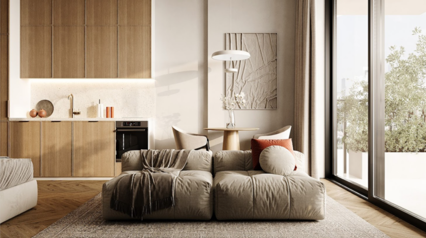Il moderno soggiorno dell'Arisha Terraces presenta un divano beige con cuscini rotondi e un plaid testurizzato. Una parete è rivestita da armadi in legno con piano di lavoro ed elettrodomestici incorporati. Nelle vicinanze si trova un piccolo tavolo da pranzo, mentre le ampie finestre offrono una splendida vista sul verde esterno.