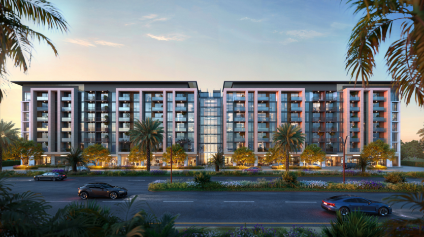 Modern six-storey twilight apartment building with large windows and balconies. Surrounded by palm trees and landscaped gardens, with a street and cars in the foreground. The sky is softly lit, suggesting sunset.