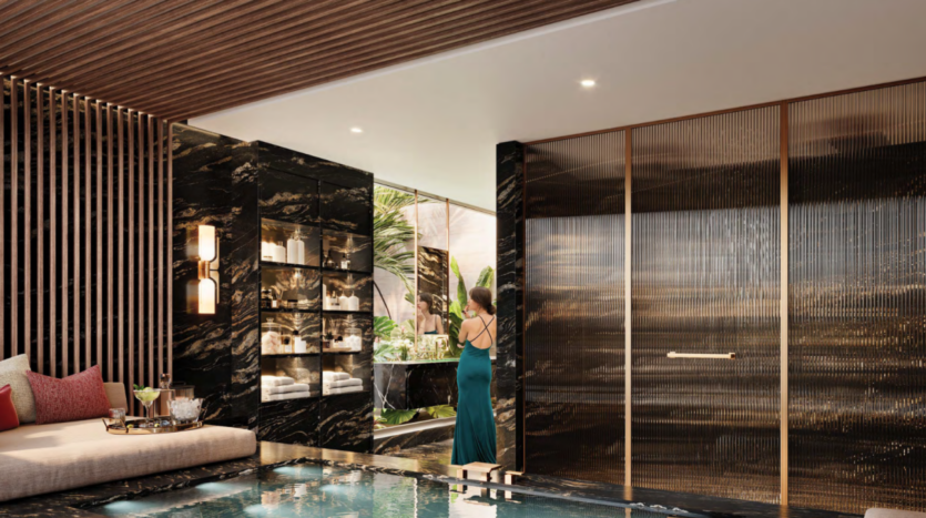 Salle de bains luxueuse avec une petite piscine, des touches de marbre foncé et un plafond en bois. Une personne vêtue d'une robe bleu canard se tient debout devant des miroirs allant du sol au plafond, faisant écho à l'essence de Bo Monde, avec des plantes tropicales visibles. Des étagères contiennent des serviettes tandis qu'une applique allumée projette une lumière chaleureuse.