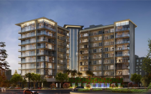 At dusk, the Floarea Grande apartment building presents itself as modern and illuminated. The structure features numerous balconies and large windows, with a landscaped entrance with palm trees and a water fountain on the first floor.