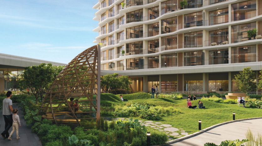 A modern urban courtyard with a multi-storey building with balconies and green spaces. People relax on the grass and stroll around. A domed wooden structure sits in the foreground, with a landscaped garden and clear skies.