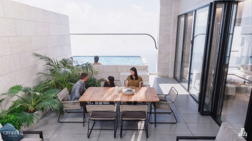 Una moderna terrazza sul tetto con un tavolo da pranzo in legno circondato da sedie. Tre persone siedono al tavolo e una in una piscina a sfioro con vista sulla città. Lo spazio è decorato con piante verdi e ha alte porte di vetro.