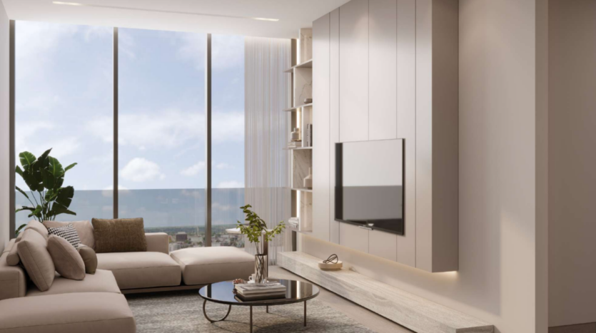 Soggiorno moderno con finestre a golfo con vista sulla città. Presenta un divano angolare beige, un tavolino rotondo con piante, una TV a parete e mobili eleganti. La luce naturale esalta il design arioso e minimalista.