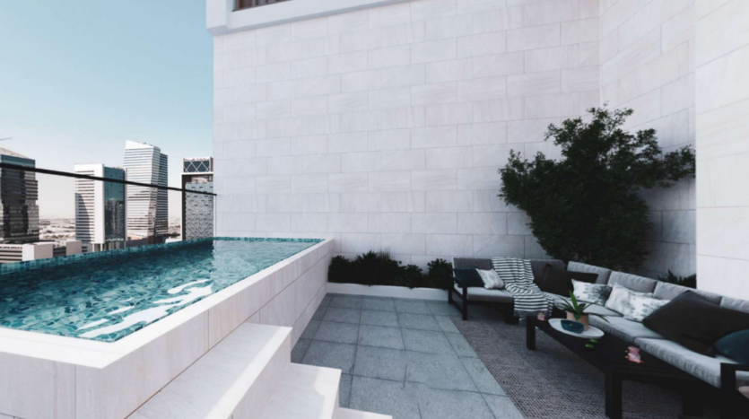 Terrazza sul tetto minimalista con piscina rettangolare dall'acqua limpida e blu. Accanto alla piscina si trova una comoda area salotto con un divano angolare grigio, cuscini a righe e un piccolo tavolo rotondo. Sullo sfondo si vede lo skyline della città.