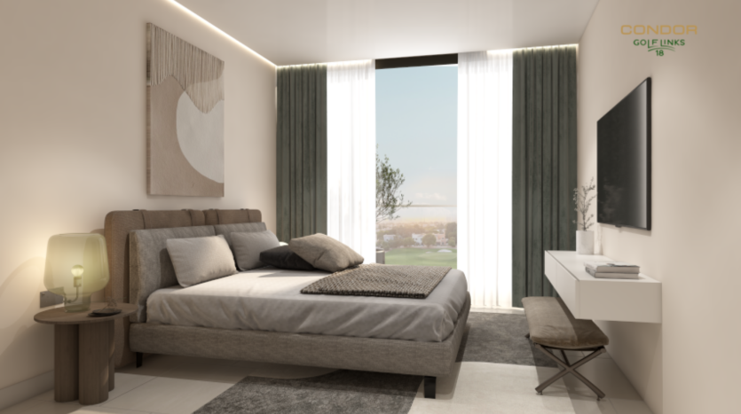 Une chambre moderne dispose d'une grande fenêtre avec des rideaux transparents, permettant à la lumière naturelle d'illuminer l'espace. La chambre comprend un lit avec une literie grise, une télévision murale et un bureau simple idéal pour suivre les parcours de golf. Une tenture murale décorative et une lampe ajoutent des touches esthétiques.
