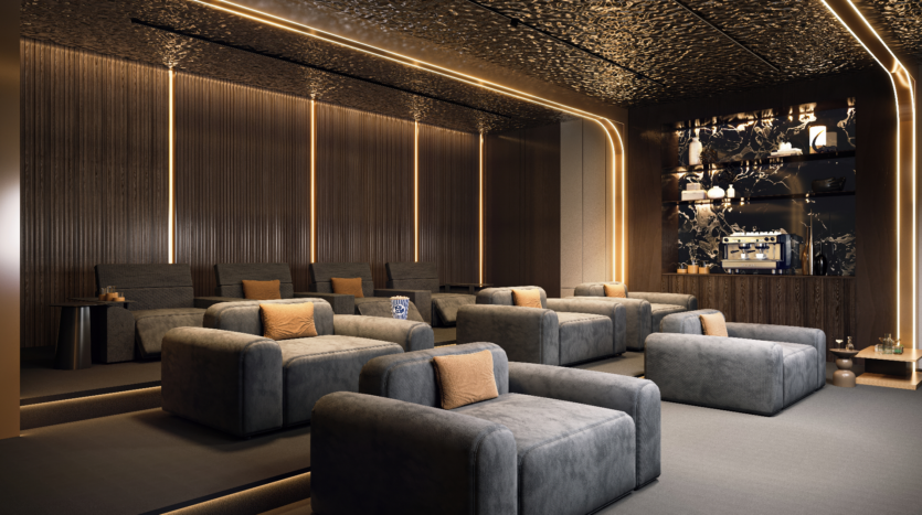 A modern, softly lit living room with Verano ambience features plush gray armchairs and warm lighting. The walls and ceiling feature a textured, dark design. In one corner, a small bar area with a coffee machine and decorative shelves adds to the sophisticated atmosphere.