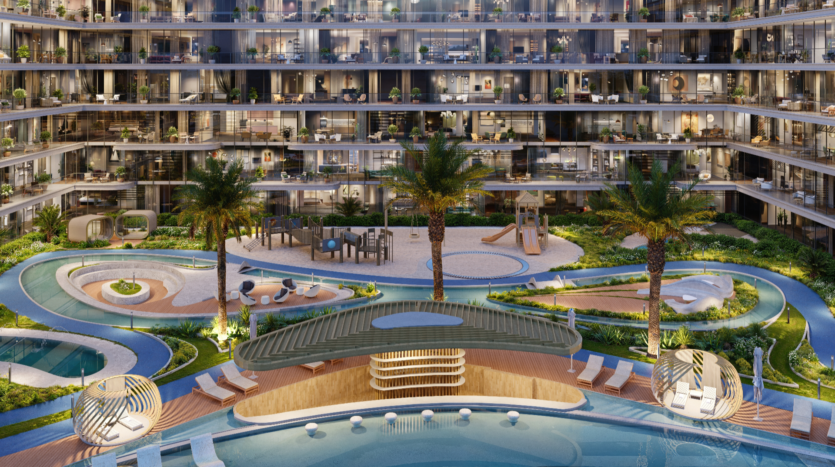 The Verano residential complex features several balconies overlooking a landscaped courtyard with a central swimming pool, playground, palm trees and winding walkways. Soft lighting illuminates the scene, creating a serene, luxurious atmosphere.