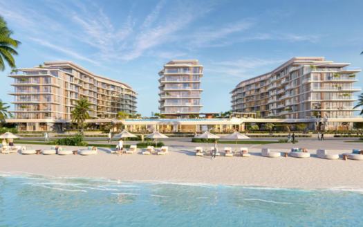 Ein Strandkomplex, der aus zwei modernen, mehrstöckigen Gebäuden besteht, die von Palmen umgeben sind. Weiße Sonnenschirme und Liegestühle sind am sandigen Ufer aufgestellt, mit den ruhigen blauen Wellen des Ozeans im Vordergrund unter einem klaren, sonnigen Himmel.