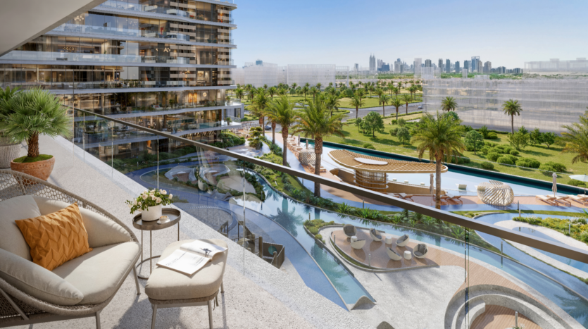 Luxurious views from the balcony of a modern Verano apartment, overlooking a landscaped garden with palm trees, sinuous pools and sun loungers. An urban skyline is visible in the distance. Furniture includes comfortable chairs, a small table and potted plants.