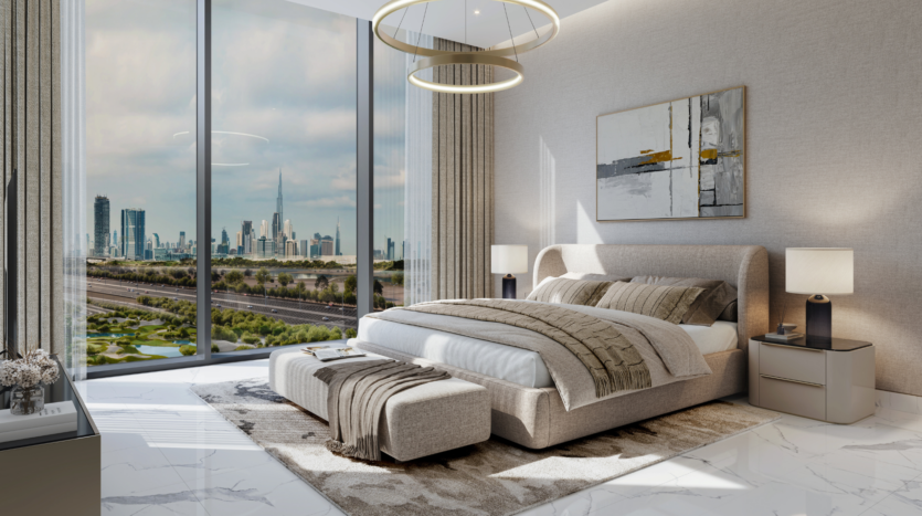 Una camera moderna con un'ampia finestra che si affaccia sui tetti della città, caratterizzata da un morbido letto con lenzuola grigie, un elegante poggiapiedi e lampade alla moda sui tavolini. Dominano i toni neutri, mentre i quadri geometrici e le plafoniere circolari della collezione Sobha One arricchiscono l'arredamento.