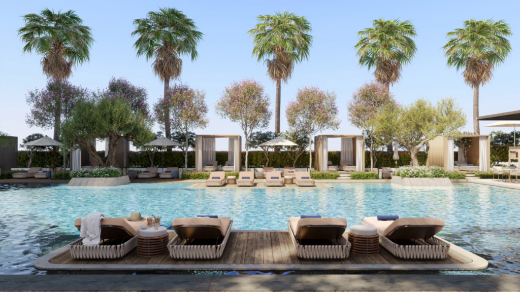 Piscine extérieure luxueuse du centre-ville de Mr C avec chaises longues et cabanons, entourée de palmiers et de plantes à fleurs. Des serviettes et un chapeau reposent sur les chaises longues, tandis que le ciel reste clair et bleu.