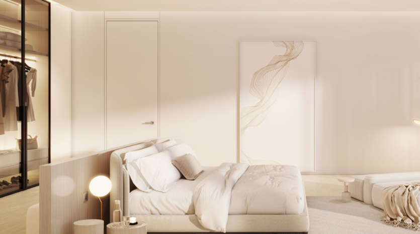 La camera da letto minimalista del Chedi Private Residences ha un letto king size con biancheria bianca. Un comodino a luce soffusa ospita una lampada sferica, mentre una fluente opera d'arte astratta accentua l'atmosfera serena. Un armadio a vista contiene abiti appesi con cura alle grucce.