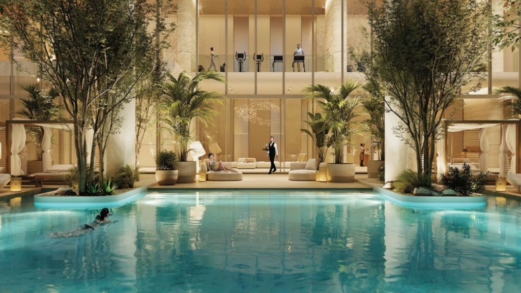 La lussuosa piscina coperta del Chedi, simbolo delle residenze private, è circondata da una vegetazione lussureggiante e da eleganti sedute. Una persona nuota tranquillamente mentre gli altri si rilassano sulle sedie. Le grandi finestre rivelano un interno spazioso e moderno con accenti in legno e luci soffuse.