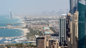Vue aérienne de l'horizon de Dubaï avec ses gratte-ciels imposants et l'emblématique Burj Al Arab sur la côte, avec une marina parsemée de bateaux. Le paysage urbain s'étend au loin sous un ciel bleu clair, créant une scène parfaite pour les acheteurs potentiels qui envisagent un bien immobilier en février 2025.