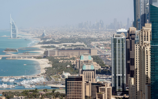 Luftaufnahme der Skyline von Dubai mit seinen imposanten Wolkenkratzern und dem ikonischen Burj Al Arab an der Küste mit einem von Booten übersäten Jachthafen. Die Stadtlandschaft erstreckt sich in der Ferne unter einem klaren blauen Himmel und schafft eine perfekte Kulisse für potenzielle Käufer, die im Februar 2025 eine Immobilie in Betracht ziehen.