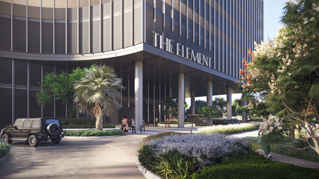 L'elegante ingresso di "The Element" è caratterizzato da grandi vetrate e colonne eleganti. Le persone si riuniscono tra il verde lussureggiante, gli alberi e un SUV nero parcheggiato nel vialetto, che riflette l'estetica moderna di Sobha One.