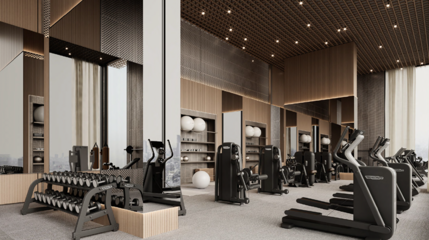 The Binghatti Skyhall's modern gym features state-of-the-art equipment, including treadmills, exercise bikes and dumbbells. It features neutral tones, large mirrors and wood accents in a bright space with a high ceiling adorned with a grid pattern.