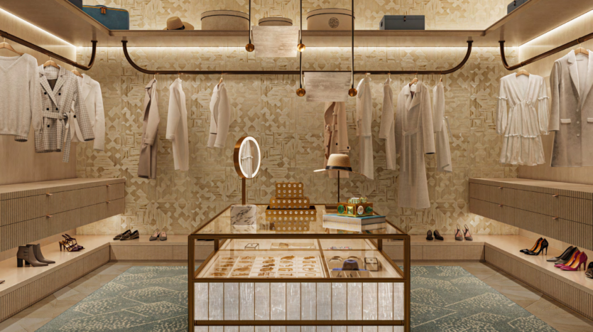 Luxurious dressing room in Asora Bay, Dubai, with beige-patterned walls and subdued lighting. Clothes are neatly hung on both sides. A central island displays jewelry. Shelves hold shoes, hats and handbags. An ornate rug lies beneath a round mirror that rests on the island.