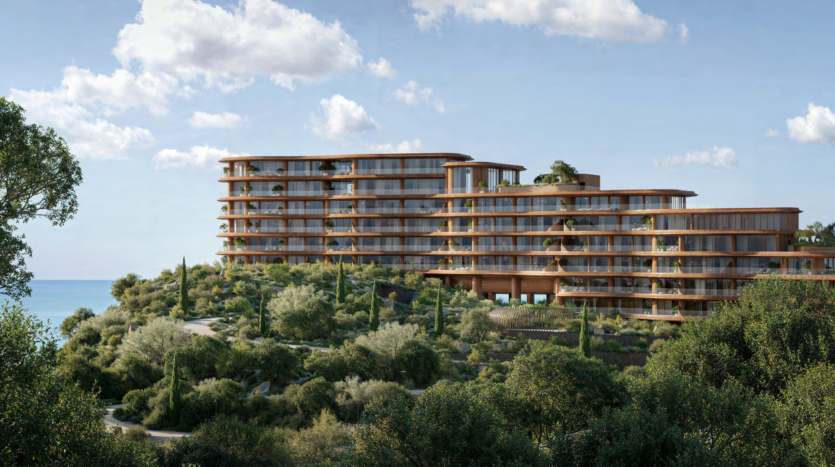 Set on a hillside, this modern Dubai hotel features elegant glass and wood panel architecture, surrounded by lush vegetation. Overlooking the tranquil Asora Bay, it offers breathtaking ocean views under partly cloudy skies.