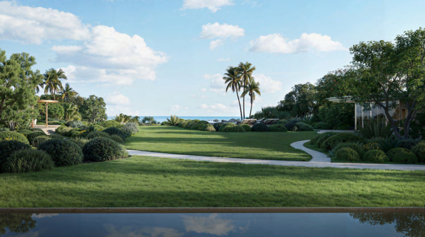 A picturesque landscape with lush green lawn, winding paths and clusters of shrubs. Palm trees dot the area, offering a serene view of Dubai's Asora Bay under a partly cloudy blue sky.