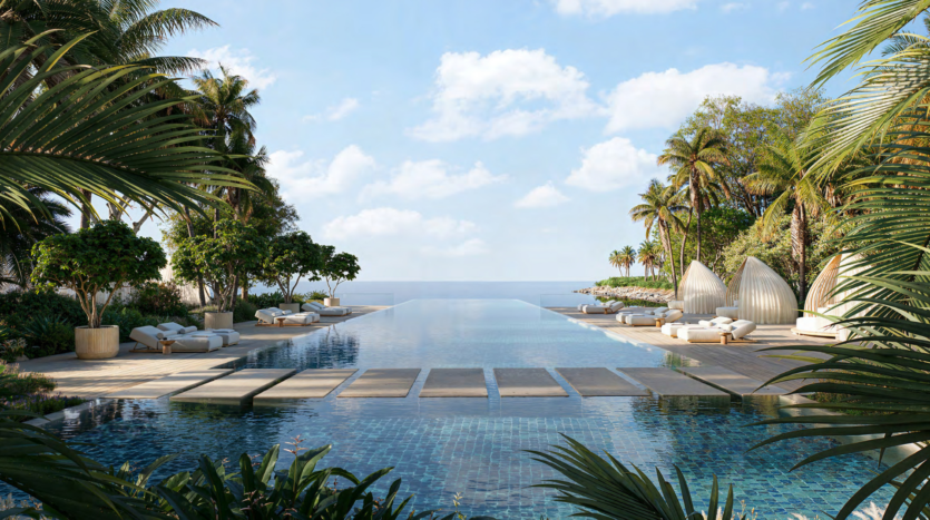 Luxurious pool area at Asora Bay Dubai, with an infinity pool that extends to the ocean. Surrounded by lush palm trees and elegant sun loungers with parasols, all set against a backdrop of bright blue skies dotted with clouds.