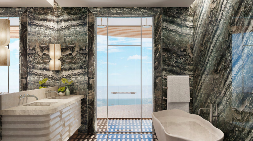 Luxurious bathroom with marble walls and floor in Dubai's famous Asora Bay. It features a freestanding bathtub, a double vanity with two lamps and a large window offering panoramic ocean views. A white towel hangs from a bar next to lush green plants.