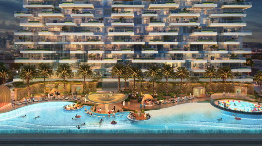A luxurious Damac condominium with balconies and green spaces, illuminated at dusk. At the front, the Safa-inspired outdoor pool features palm trees, lounge chairs and people swimming around a circular platform in the center.