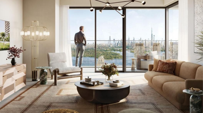 Una persona si trova davanti alla finestra di un soggiorno moderno, con vista sulla città, i suoi grattacieli e un fiume. L'ambiente è arredato con un divano elegante, un tavolino originale, un lampadario moderno e una lampada decorativa in toni caldi e neutri.