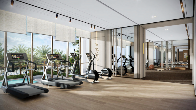 A modern gym in the Atelis design district, with large windows offering panoramic views of the outside. The room is equipped with several treadmills, elliptical bikes and rowing machines, set on a light parquet floor. Mirrors adorn the walls, reflecting both the equipment and the magnificent outdoor landscape.