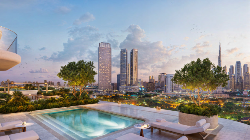 A rooftop infinity pool, complete with sun loungers, overlooks the city at sunset, in the Atelis design district. Two lush trees line the pool, while skyscrapers, including a tower with a spire, dominate the background under a partly cloudy sky.