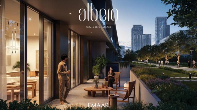 Due persone chiacchierano su una moderna terrazza con vista su un parco paesaggistico e sui tetti della città al tramonto. Gli eleganti arredi da esterno e l'illuminazione calda creano un'atmosfera accogliente. Un logo in alto recita "Albero, Dubai Creek Harbour, Emaar".