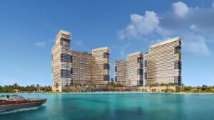 Una vista mozzafiato del lungomare di Damac Maritime City mette in evidenza tre moderni grattacieli con linee verticali distinte e tetti verdi. In primo piano, un motoscafo scivola sull'acqua turchese, mentre il cielo limpido è punteggiato solo da qualche nuvola.