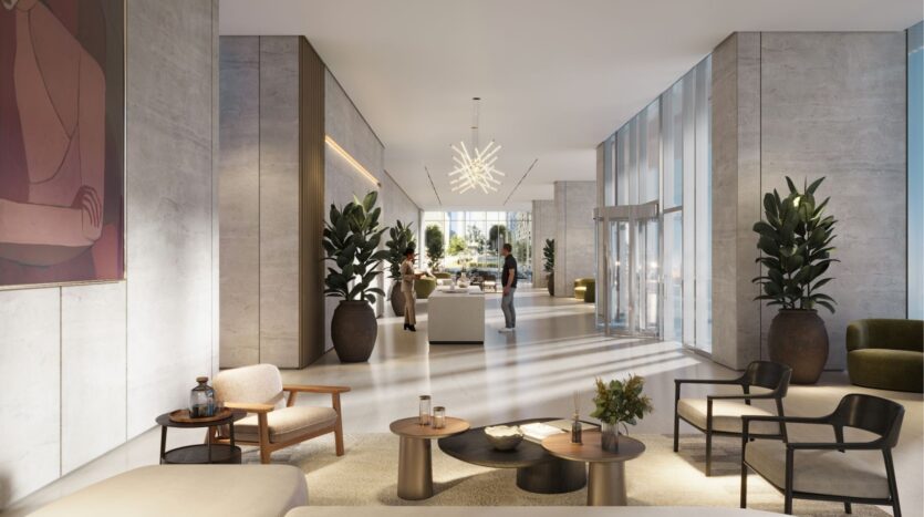 In the chic lobby of DIFC Heights, high ceilings and large windows welcome visitors to a space adorned with elegant furnishings and lush plants. A contemporary chandelier adds a touch of elegance, while passers-by bustle in the background near the entrance.