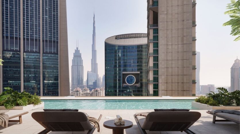 The rooftop pool, equipped with two sun loungers and towels, overlooks the city, with its towering skyscrapers and the iconic Burj Khalifa in the background. The landscape is beautifully framed by the heights of the DIFC and the surrounding greenery.