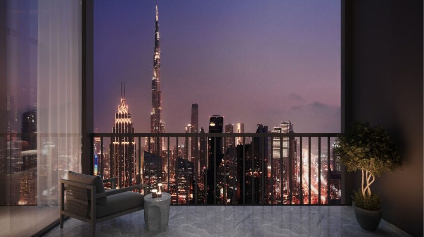 At night, a modern balcony overlooks the skyscrapers of DIFC Heights, showcasing a tall illuminated skyscraper and other illuminated buildings. A chair and a small table with a green plant enhance the peaceful urban setting.